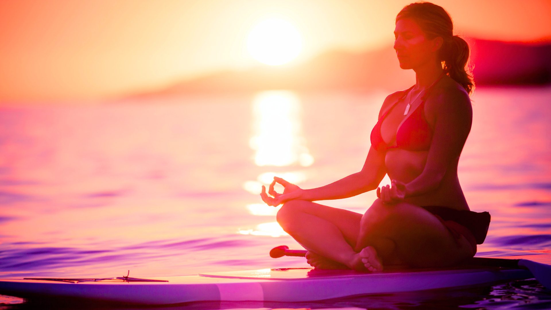 Woman on paddleboard meditating on water at sunset
